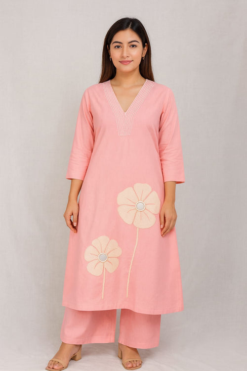 Model wearing a blush pink kurta and palazzo set with pintuck V-neckline and floral mirror-work appliqués